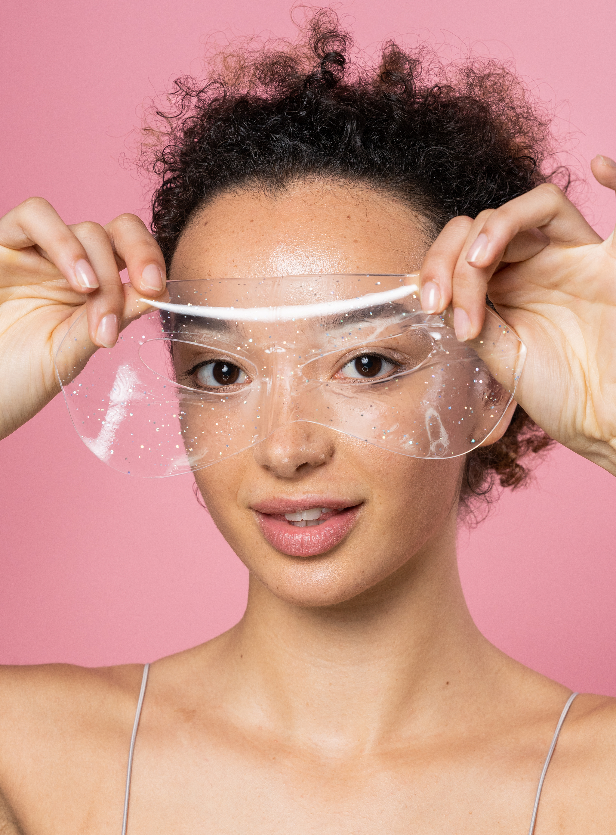 Woman holding a clear face shield against a pink background