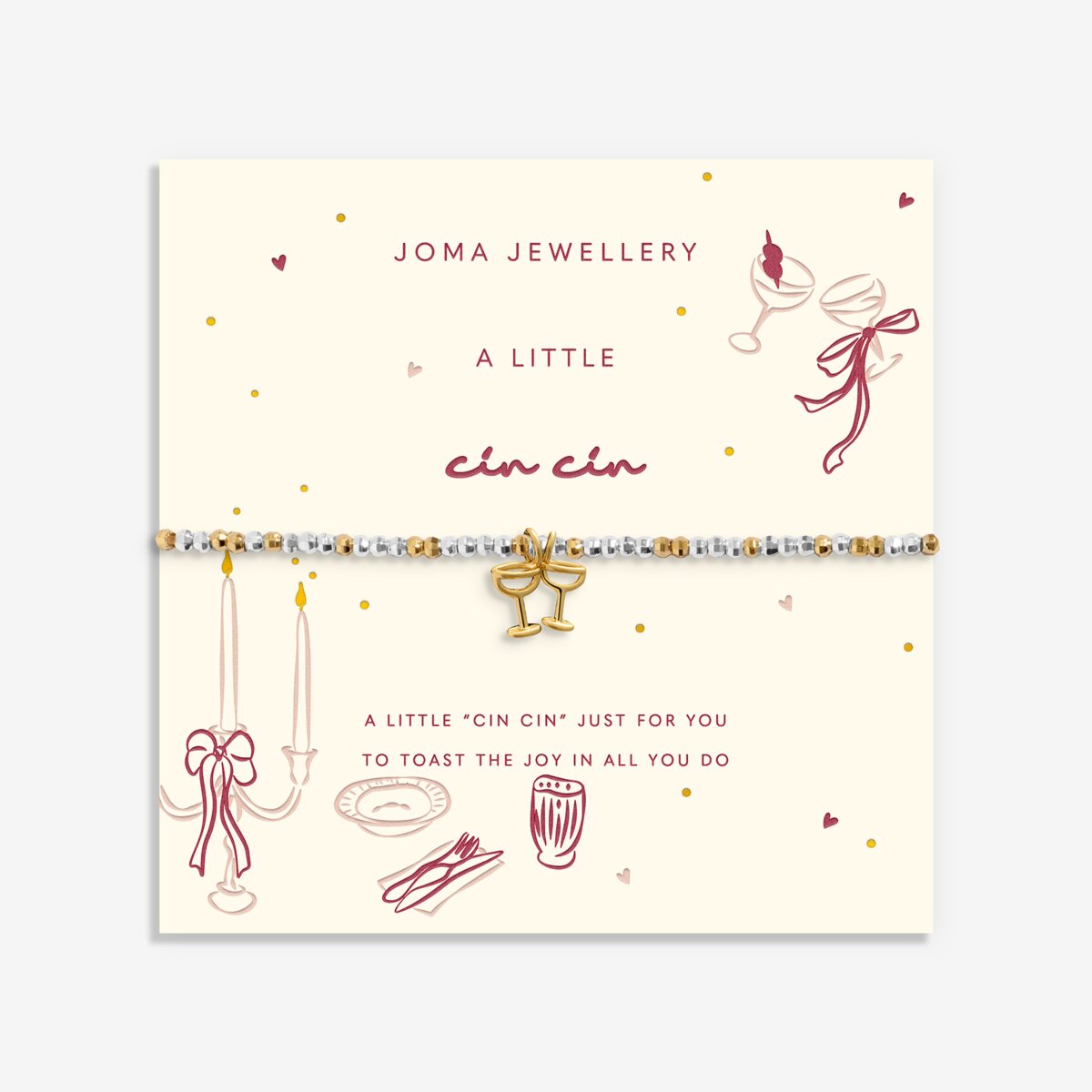 A beaded bracelet with a gold bow charm displayed on a cream-colored Joma Jewellery card. The bracelet features white and gold beads with a central gold bow charm.