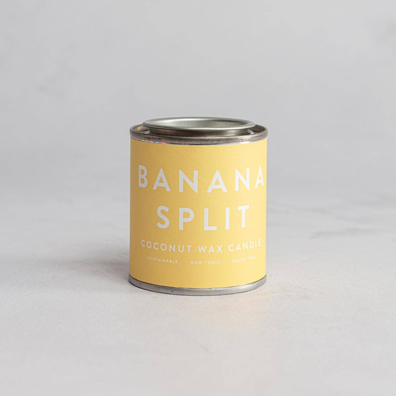 A can of Banana Split coconut wax candle with a yellow label on a neutral background.