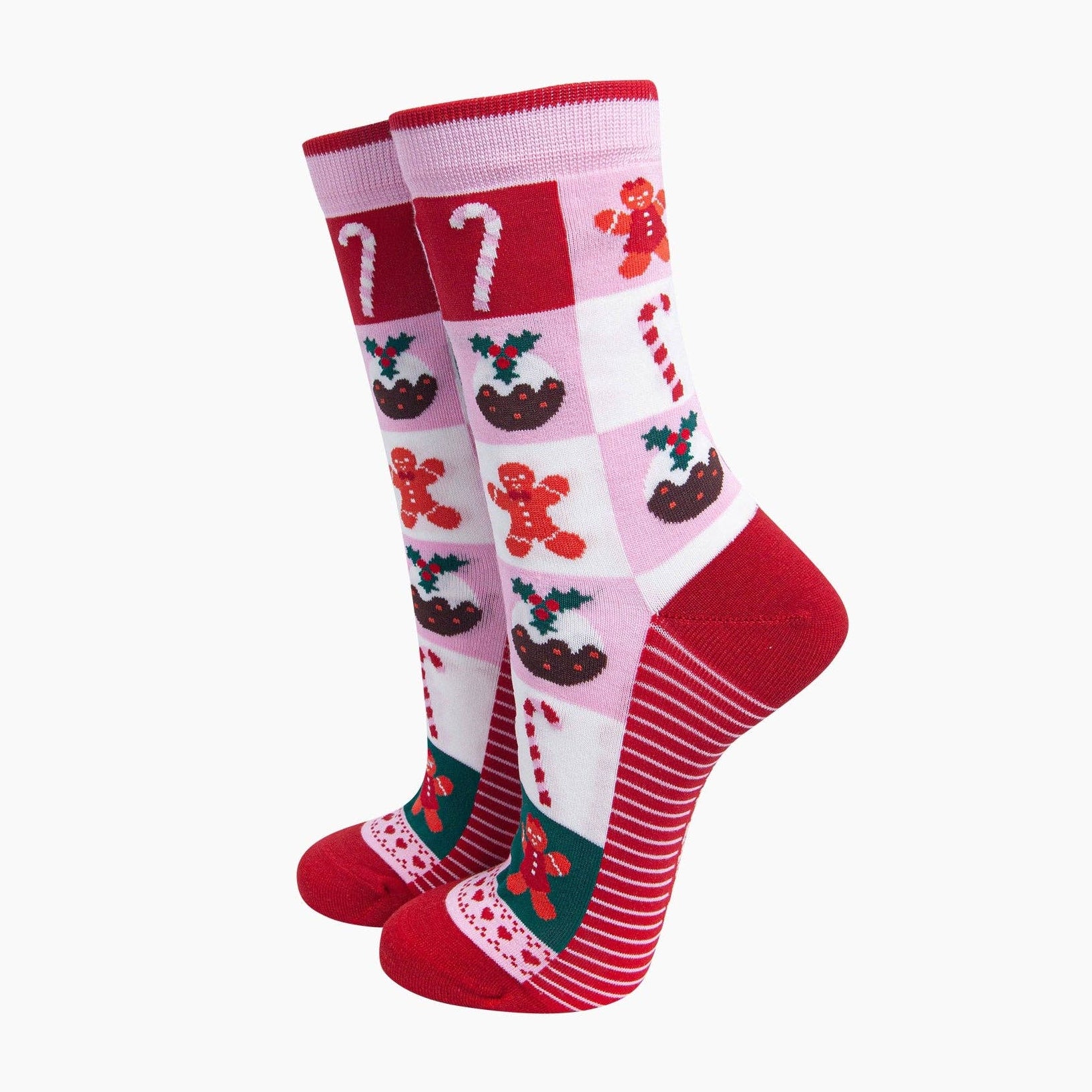 A pair of Christmas-themed crew socks featuring a pink and white checkered pattern with gingerbread men, candy canes, and mulberries, accented with solid red heels, toes, and cuffs.