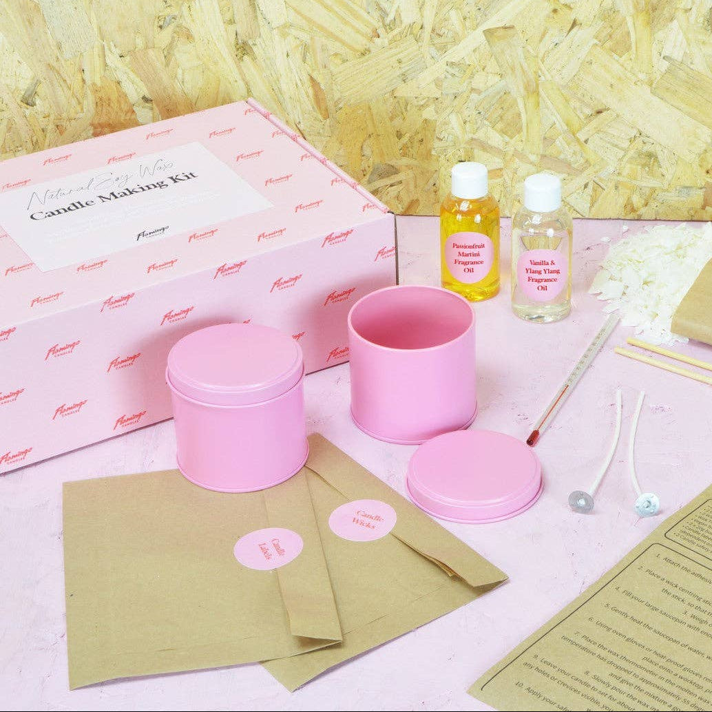 Candle making kit with pink containers, bottles, and instructions on a textured surface.