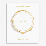 A Joma Jewellery 'Wifey' bracelet displayed on a white branded card. The bracelet features natural shell beads with small gold charms, including a heart and a square charm, and is presented on a clean white background.