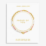 A Joma Jewellery 'Proud of You' beaded bracelet displayed on its white presentation card, featuring gold letter beads spelling 'LOVE' and a gold heart charm, with pink and white beads.
