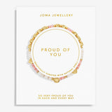 A Joma Jewellery 'Proud of You' beaded bracelet displayed on its white presentation card, featuring gold letter beads spelling 'LOVE' and a gold heart charm, with pink and white beads.