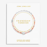 A Joma Jewellery 'Friendship Forever' bracelet displayed on its white presentation card. The bracelet features peach-pink beads, silver-toned shell charms, and a silver heart-shaped charm, arranged in a circle on the card with gold text.