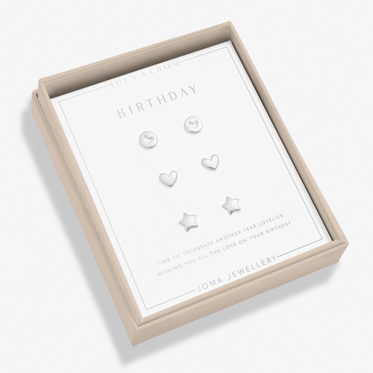 A boxed set of four silver stud earrings displayed on a white card inside a beige presentation box. The earrings include oval, heart, and star shapes, and the card reads 'BIRTHDAY' with 'JOMA JEWELLERY' at the bottom.