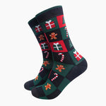 A pair of crew socks with a festive Christmas checkerboard pattern featuring red, dark green, black, white, and gingerbread men motifs, shown on a plain light gray background.