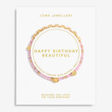 A Joma Jewellery 'Happy Birthday Beautiful' bracelet gift set on a white display card. The set features a pink beaded bracelet with gold cube charms, a pink beaded bracelet with gold heart charms, and a gold chain bracelet with gold cube charms, all arranged on a white card with gold lettering.