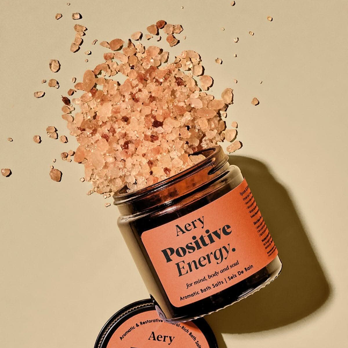 Aery Positive Energy bath salts jar with scattered bath salts on a beige background