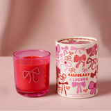 Pink candle in a glass holder next to a white candle with pink bow design on a pink background