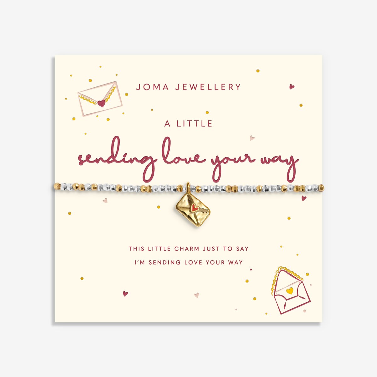 A Joma Jewellery bracelet on a cream gift card. The bracelet features a gold charm with a red heart and a silver and white beaded band.