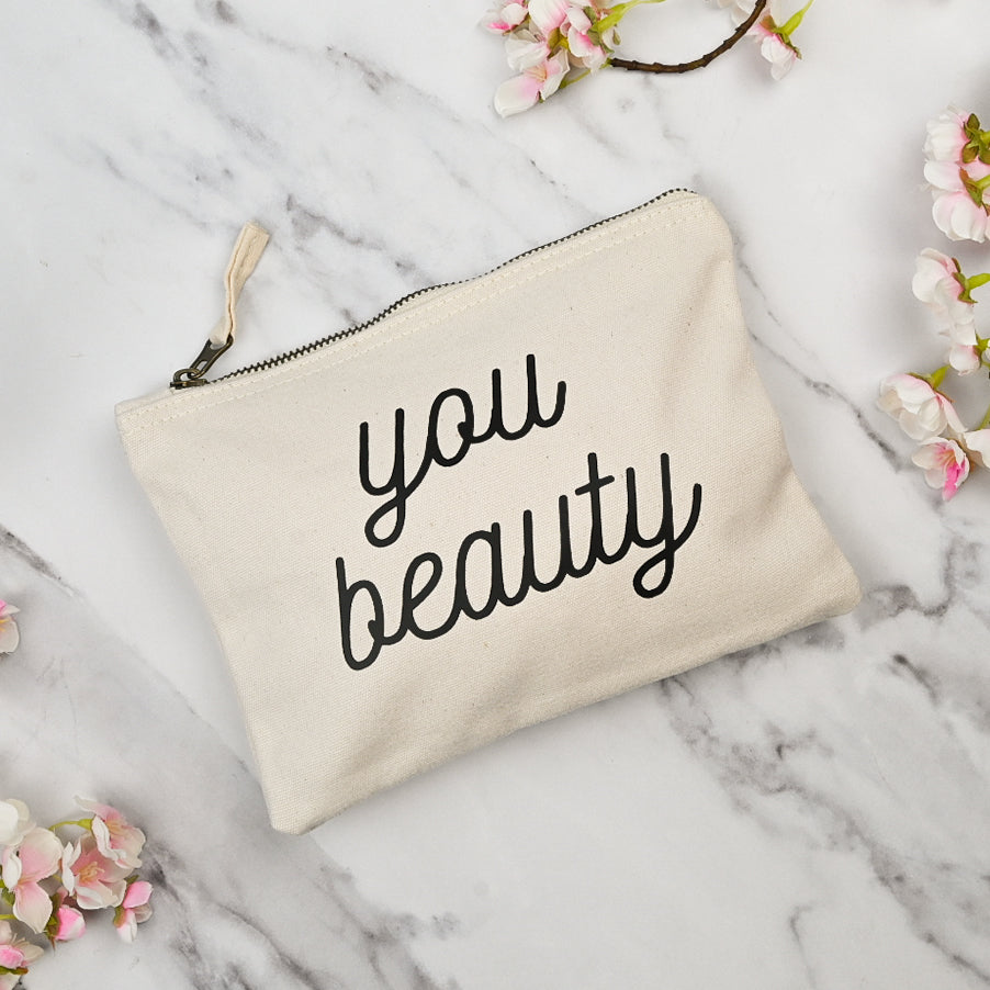 Beige pouch with 'you beauty' text on a marble surface with flowers