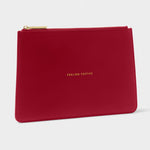 A red textured leather zip pouch with gold lettering that reads 'FEELING PERFECTIVE' and a gold zipper, shown on a light gray background.