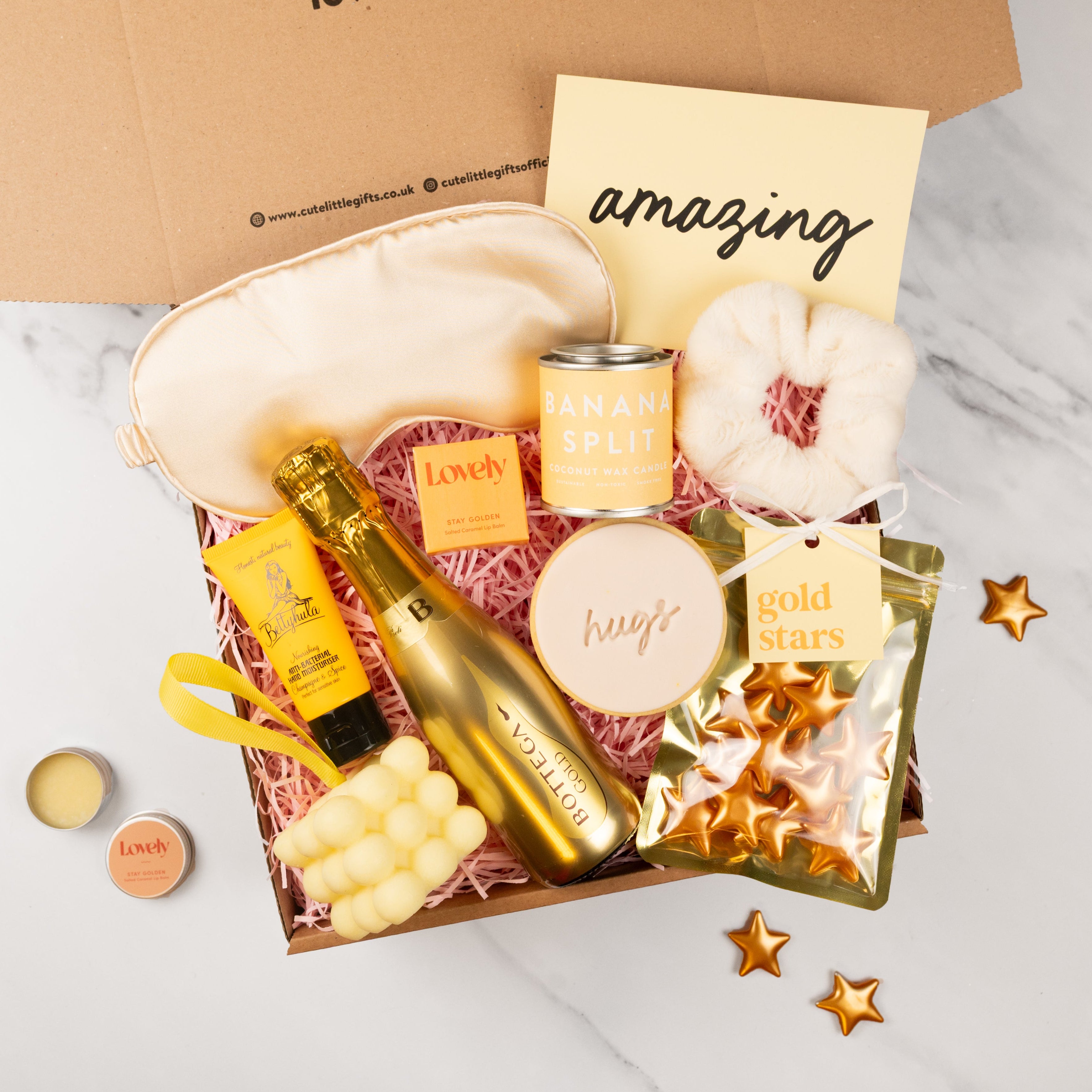 Gift box with champagne, snacks, and decorative items on a marble surface